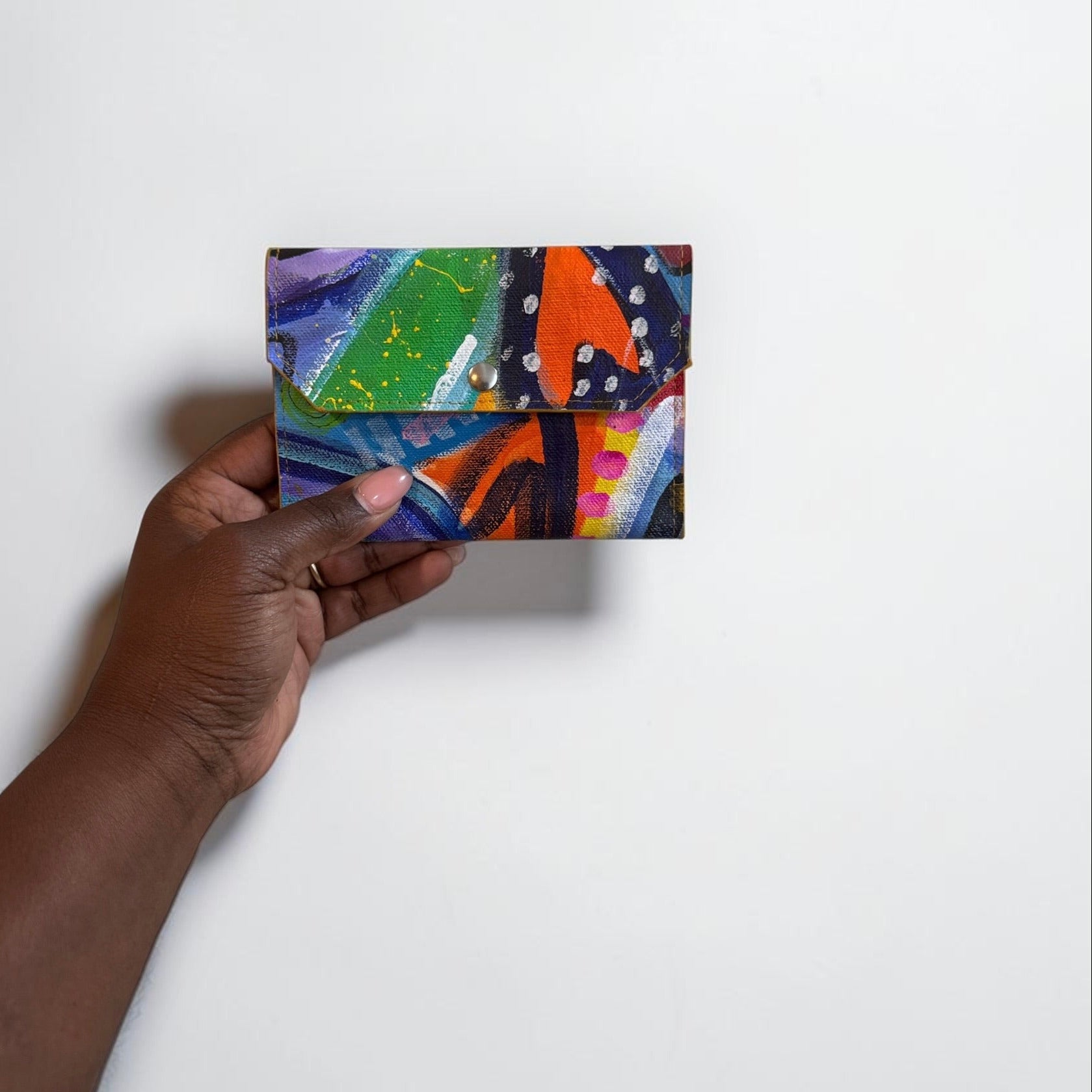 Hand holding a colorful abstract painting wallet against a white background
