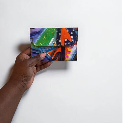 Hand holding a colorful abstract painting wallet against a white background